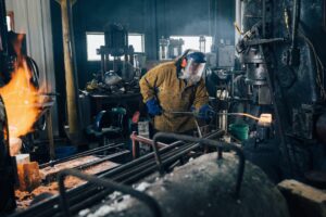 Blacksmith shaping red hot metal rod in workshop