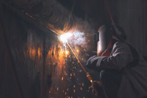 welder using arc welding machine to welding metal wall of the old vessel at shipyard in dark tone